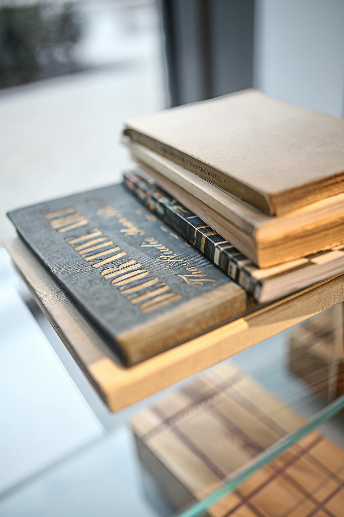 A close-up photo of vintage books stacked on a glass table indoors.